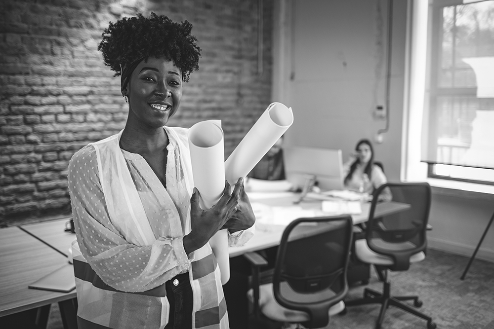 Woman smiles holding blueprints from her construction company knowing they can finance their construction invoices.