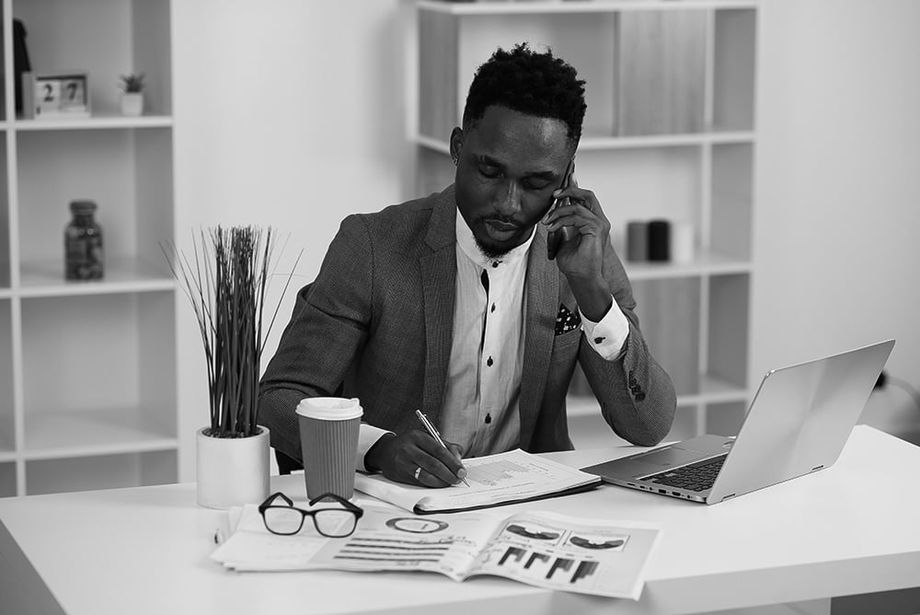 businessman behind laptop writes notes on a spreadsheet while talking on a mobile phone