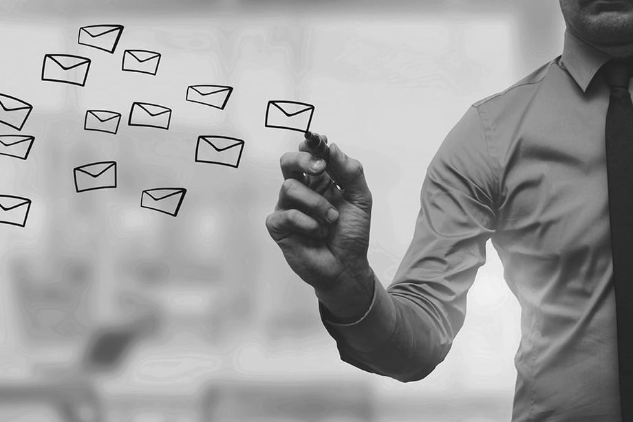 businessman in shirt and tie behind glass wall draws email symbol envelopes with a dry erase pen.