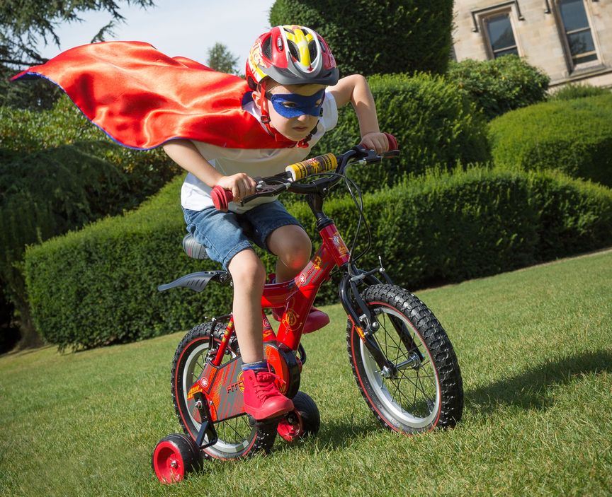 Kid on a bike with a superhero cape pretending to fly