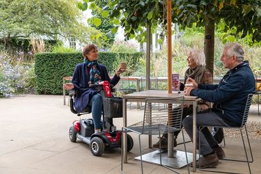 An elderly woman sitting on a mobility scooter at a table with her friends
