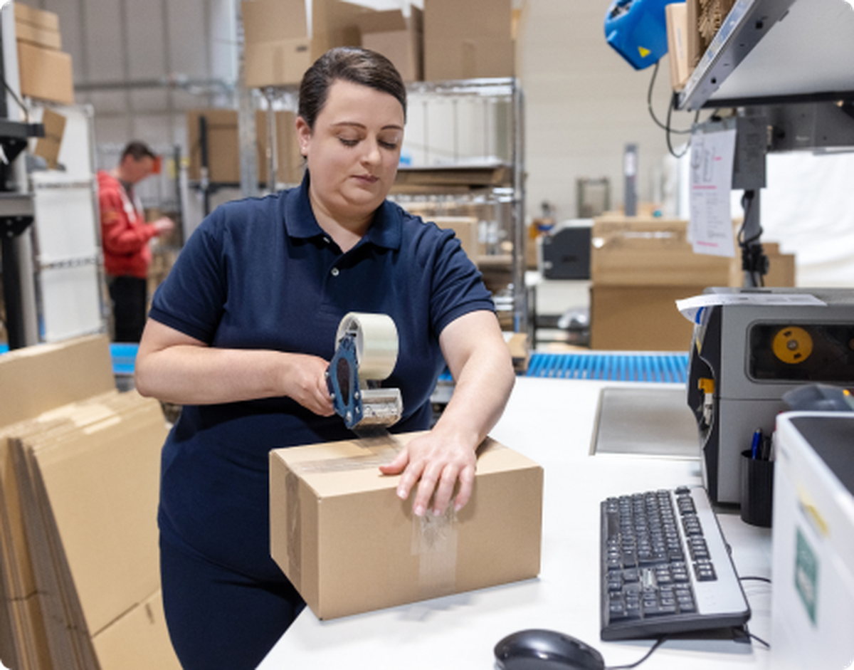 woman tapes shut a box in a warehouse setting
