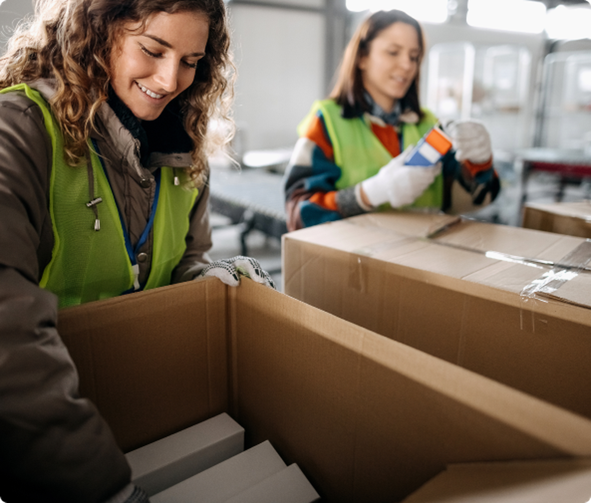 two workers in bright vests pack boxes while smiling