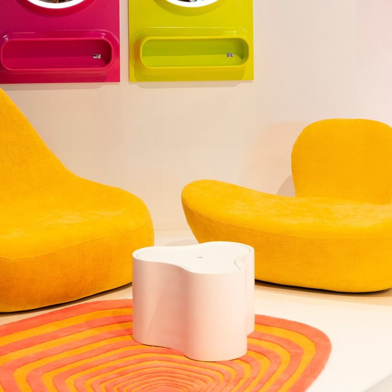 Zwei leuchtend gelbe Lounge-Sessel mit geschwungenen Formen, orangem Teppich und bunten Wandelementen.