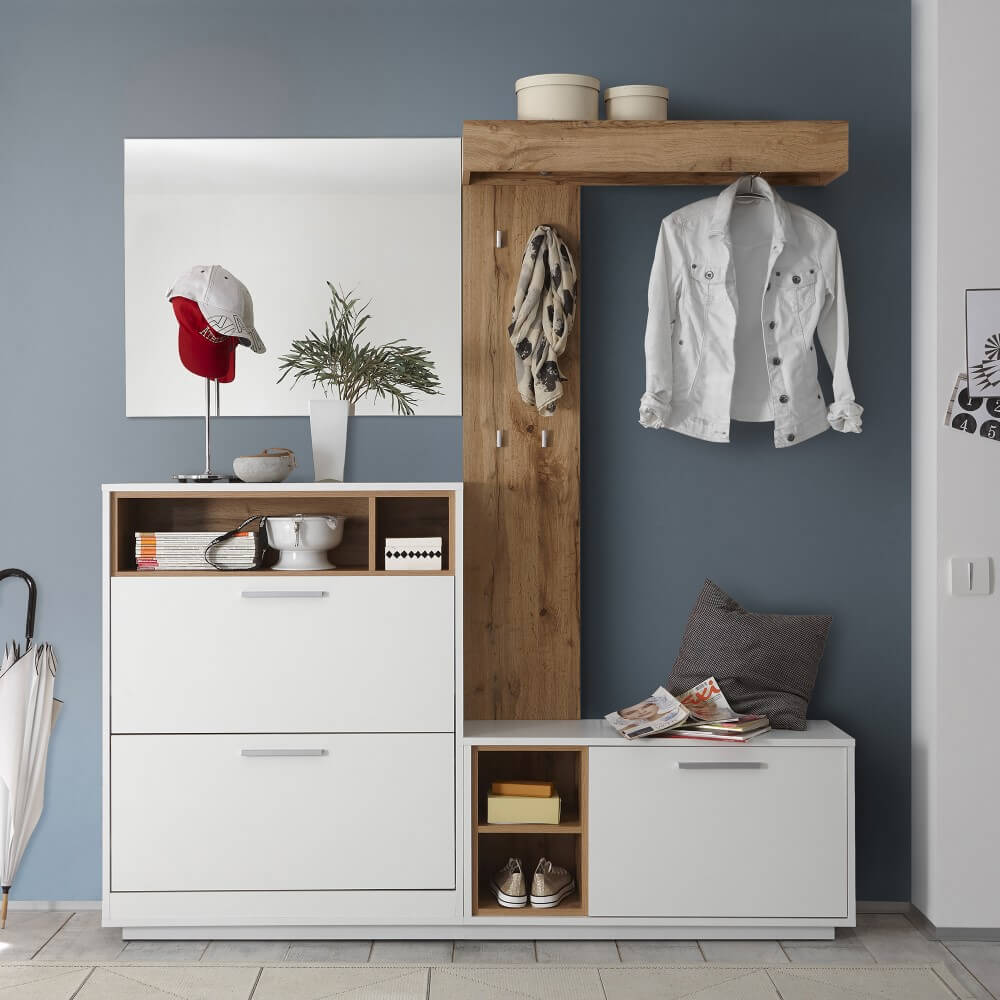 Moderner Eingangsbreich mit einer weißen Garderobe, Spiegel und dekorativen Gegenständen wie einer Pflanze, einem Hut und Schuhen vor einer blauen Wand.