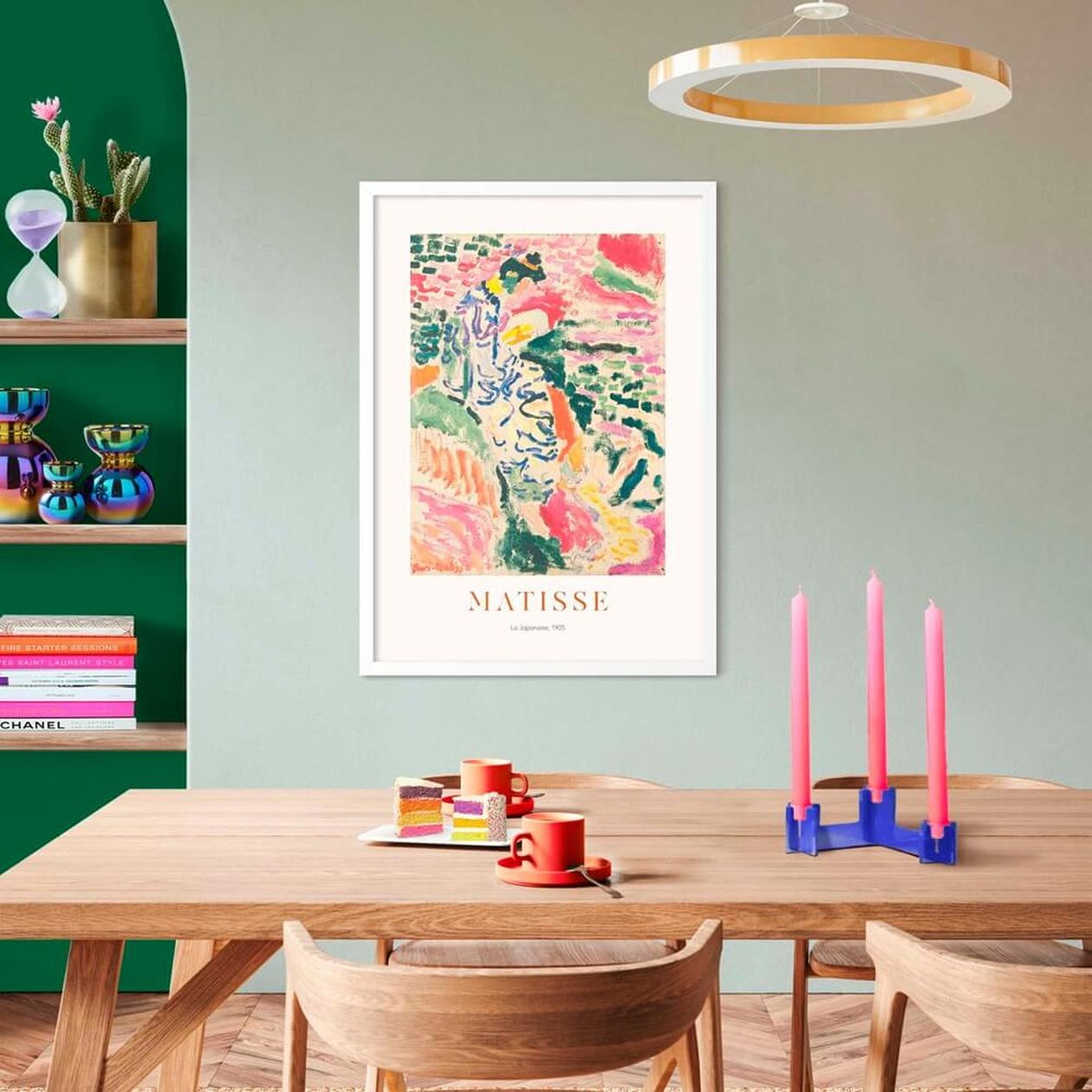 Gerahmtes Matisse-Kunstposter „La Japonaise" an einer salbeigrünen Wand über einem Holzesstisch mit Kerzen und Kaffeetassen, darüber eine goldene Ringleuchte.
