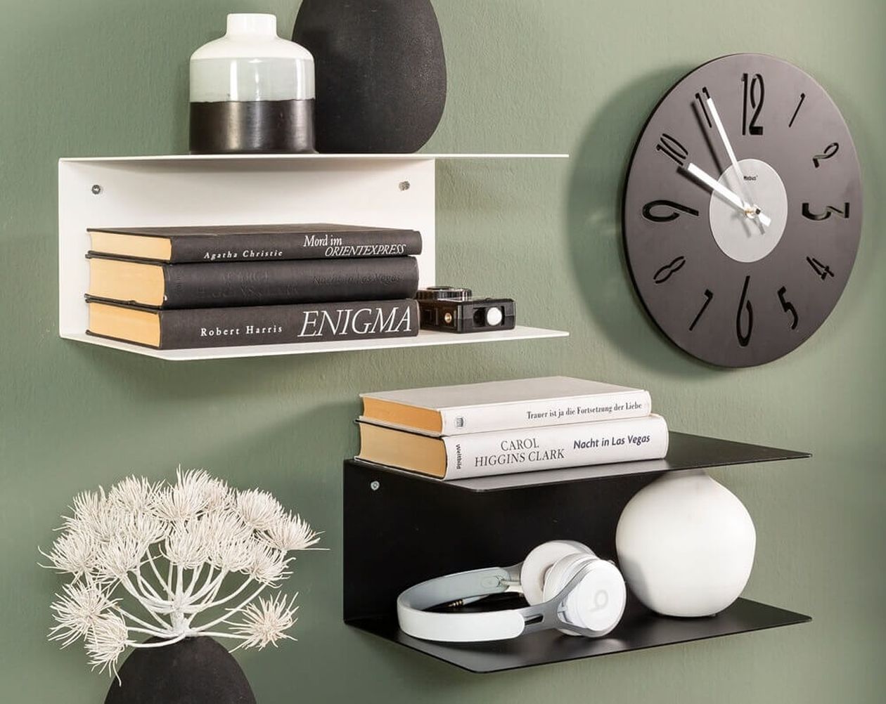 Zwei minimalistische Wandregale in Weiß und Schwarz mit Büchern, Deko-Vasen, Kopfhörern und einer schwarzen Wanduhr auf grüner Wand.