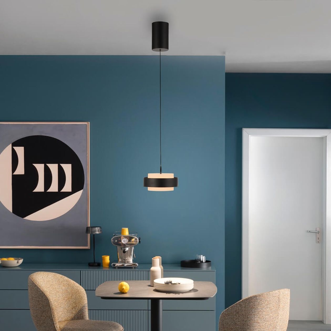 Schwarze LED-Pendelleuchte schwebt über einem modernen Essbereich mit blauen Wänden und grafischem Wandbild.