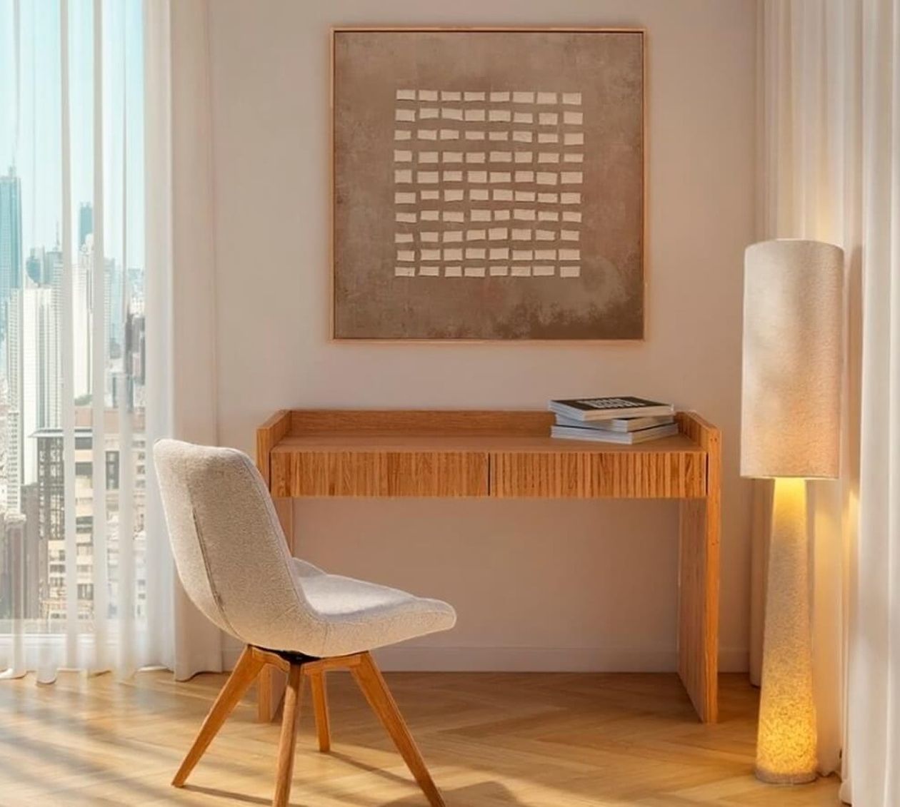 Abstraktes Wandbild mit beigem Hintergrund und Raster aus hellen Rechtecken über einem Holzschreibtisch mit Bouclé-Stuhl und zylindrischer Stehleuchte.