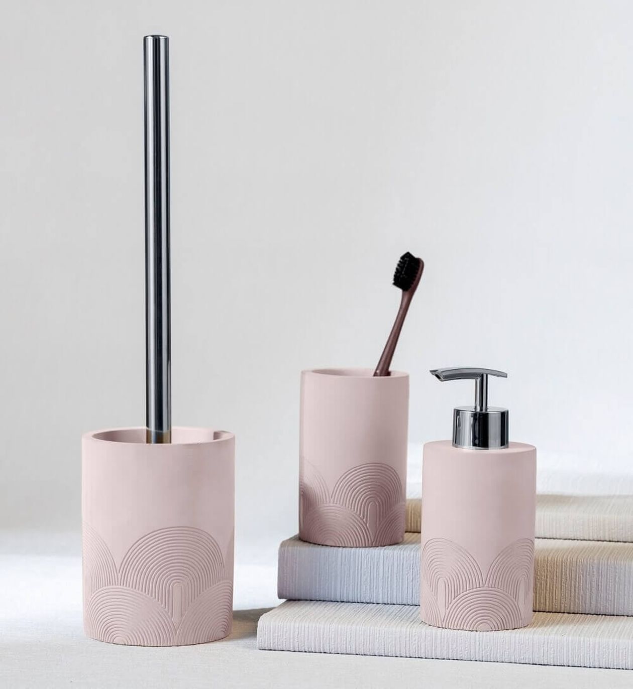 Rosa Badezimmer-Set mit geometrischen Mustern, einschließlich eines Toilettenbürstenhalters, eines Zahnputzbecherhalters mit einer schwarzen Zahnbürste und eines Seifenspenders.