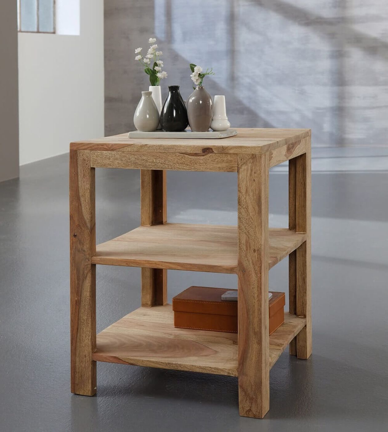 Holz-Beistelltisch mit zwei Regalen, auf denen ein Tablett mit kleinen Vasen und einer braunen Schachtel steht. Der Raum hat grauen Bodenbelag und einen hellen Hintergrund.