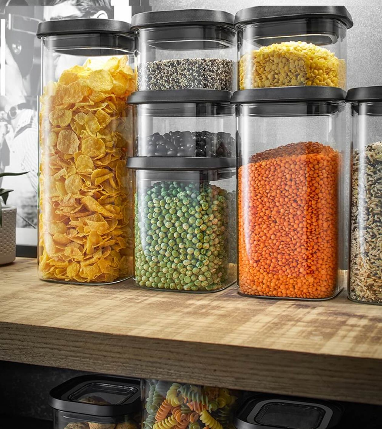 Auf einem Holzregal angeordnete, durchsichtige Behälter mit verschiedenen Trockennahrungsmitteln, darunter Cornflakes, Getreide und Linsen.