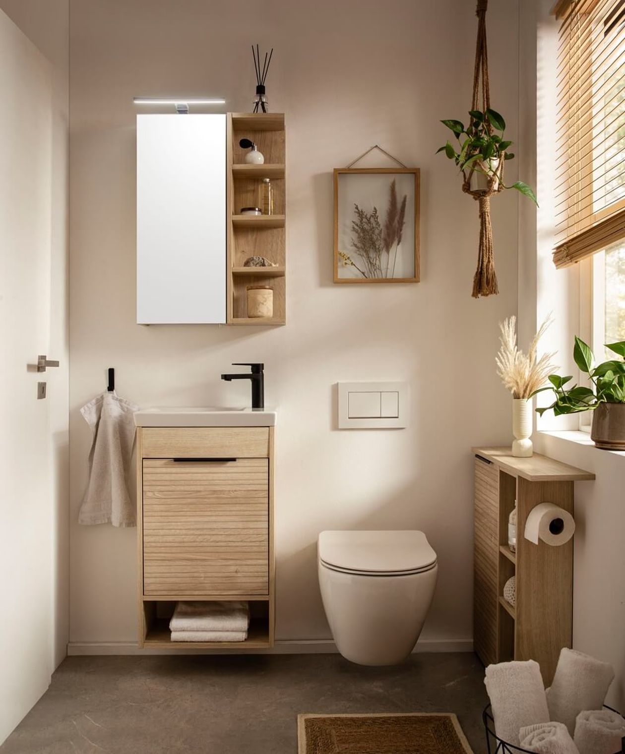 Kompakter Waschtischunterschrank in heller Holzoptik mit weißem Waschbecken und schwarzer Armatur in einem kleinen Badezimmer mit Spiegelschrank und natürlicher Dekoration.
