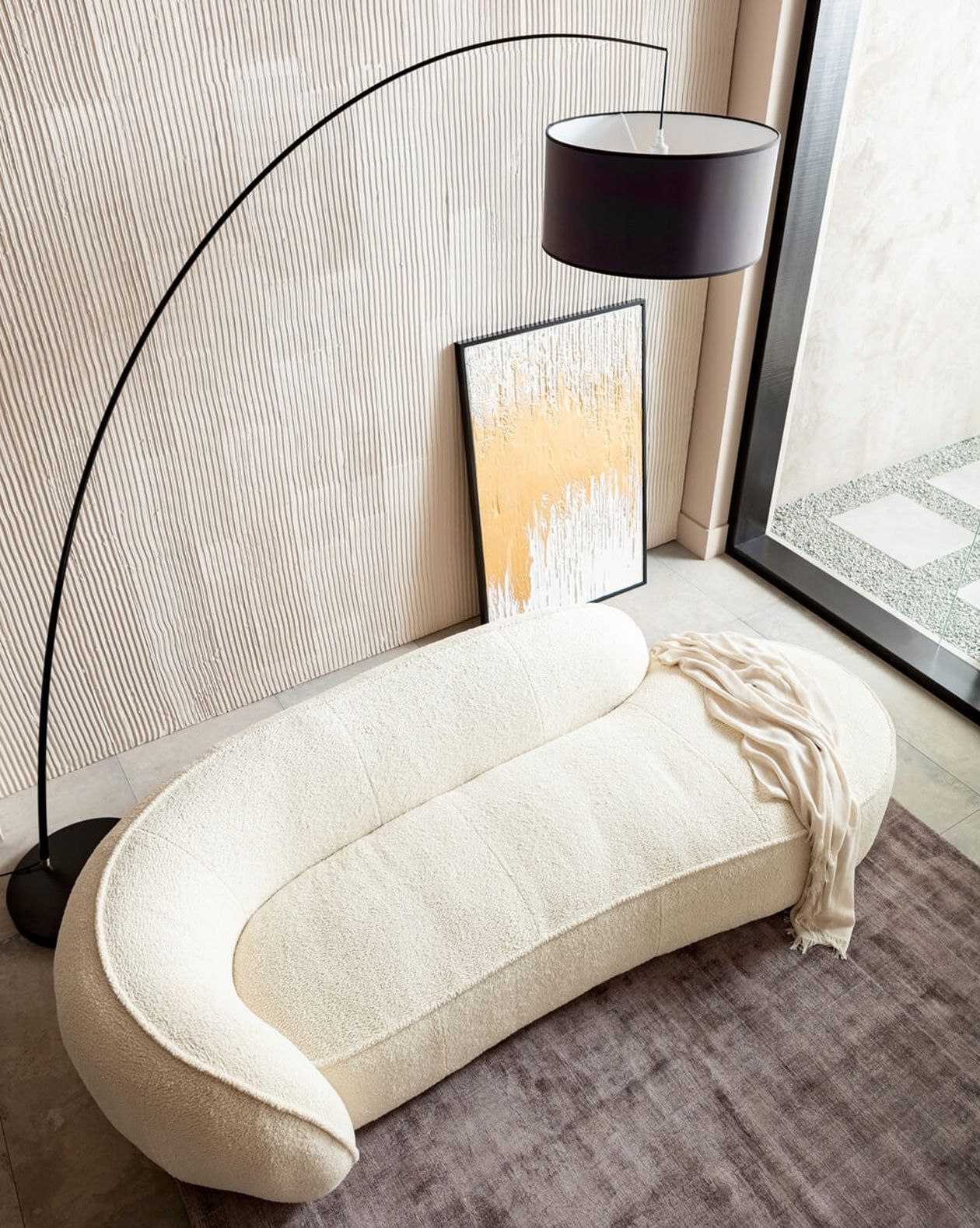 Elegante, weiße Recamiere mit fließender Silhouette neben Stehlampe und Bild, aufgenommen von oben.