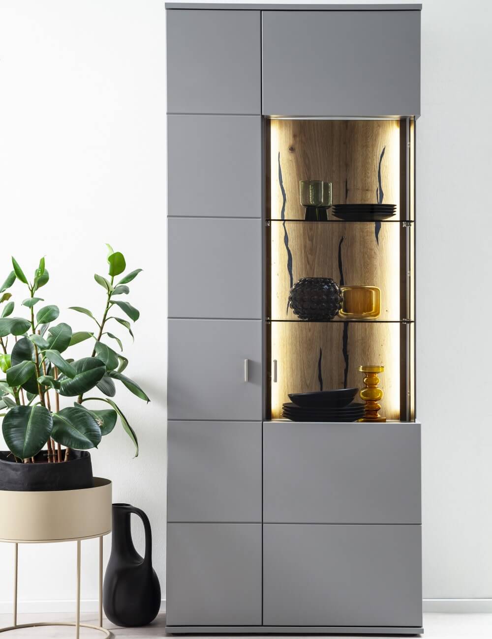 Vitrine Sevilla von mca in Grau. Hinter beleuchtetem Glas finden sich Geschirr wie Teller.