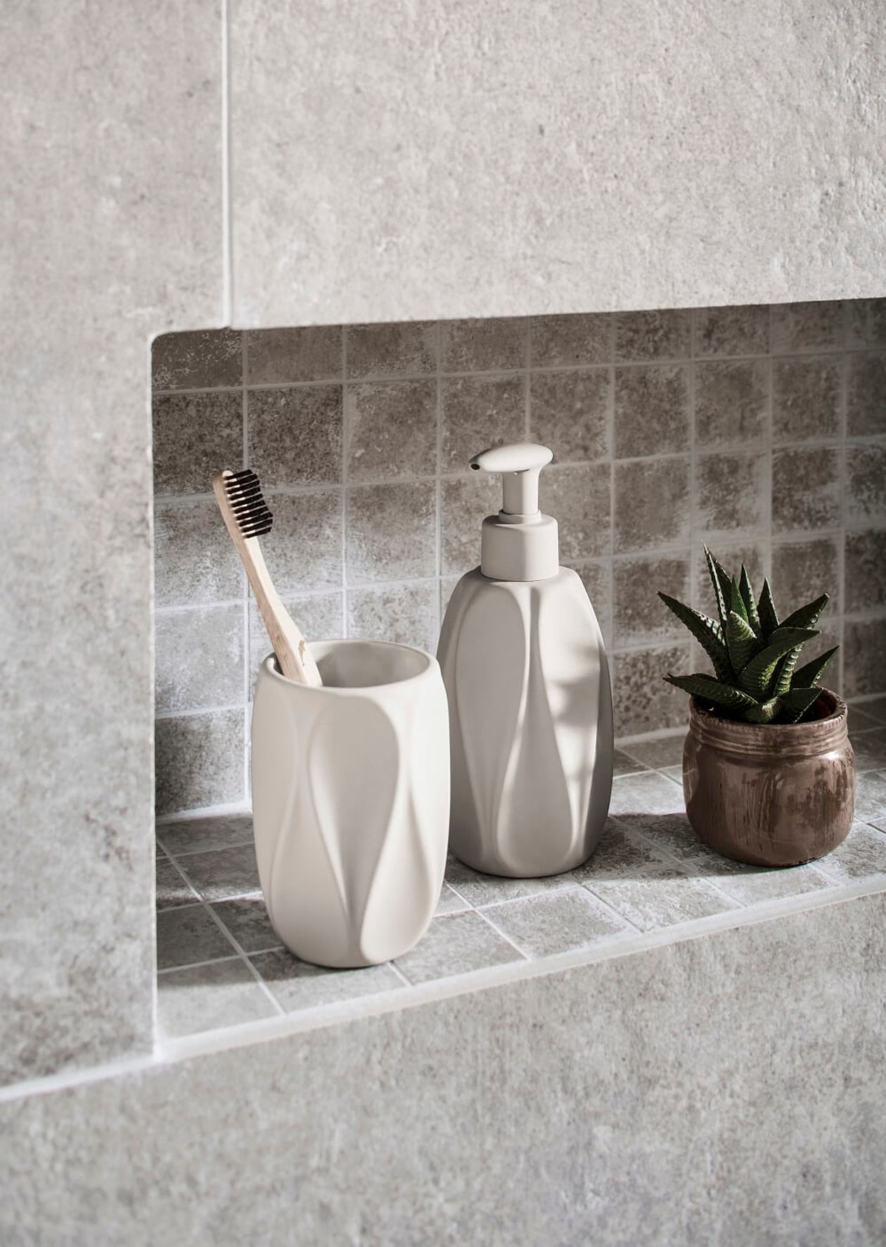 Keramik-Zahnbürstenhalter und Seifenspender auf einem gefliesten Regal mit einer kleinen Sukkulente in einem Topf.