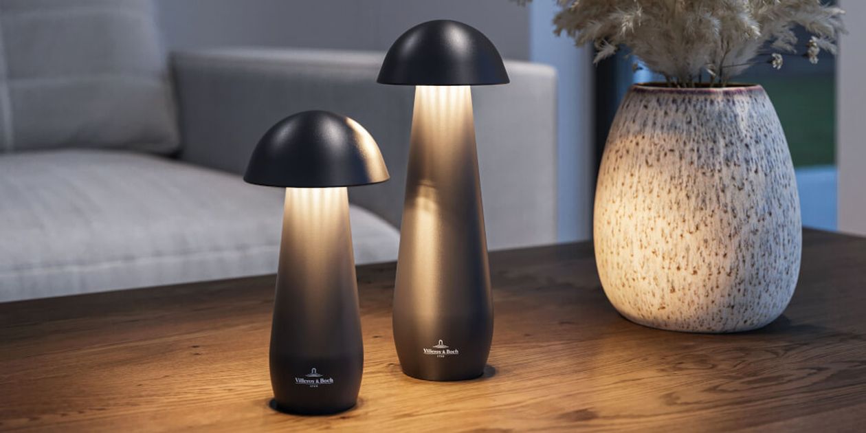Zwei moderne pilzförmige Lampen auf einem Holztisch, neben einer großen gesprenkelten Vase mit Trockenblumen, in einer gemütlichen Wohnzimmerumgebung.