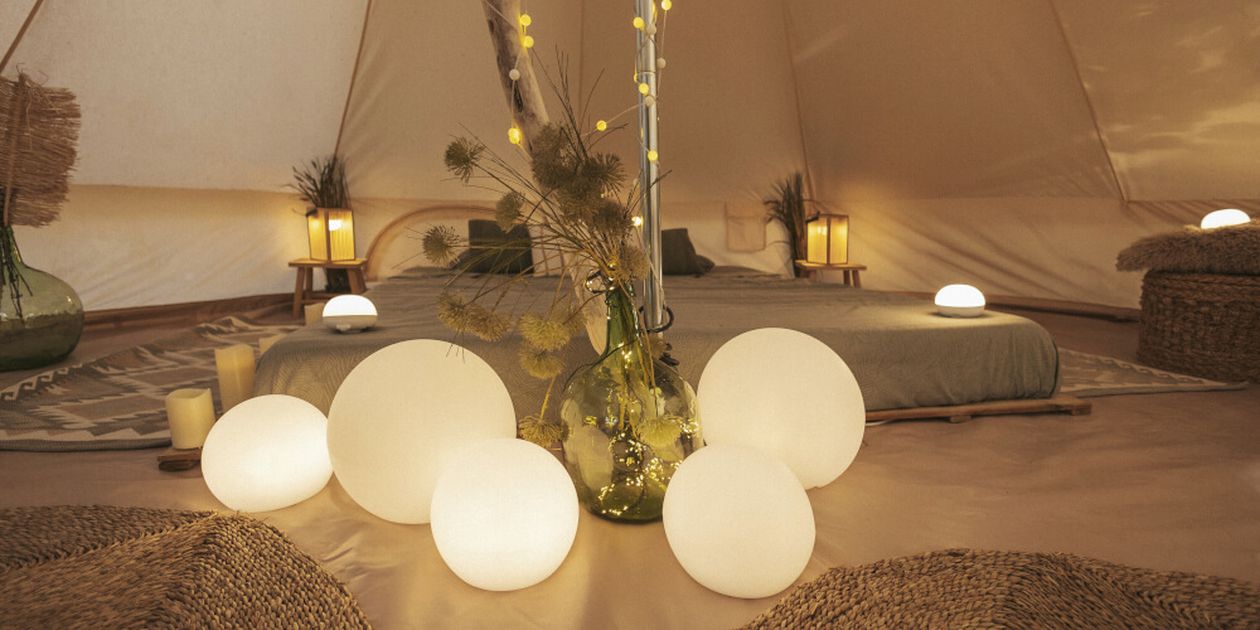 Gemütliches Zeltinterieur mit leuchtenden Kugellampen, niedrigen Betten und sanfter Beleuchtung, die eine warme und einladende Atmosphäre schaffen.