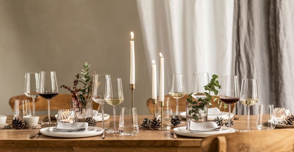 Elegantes Esstischset mit Weingläsern, Kerzen, Tannenzapfen und Eukalyptus auf einem Holztisch, das eine gemütliche, festliche Atmosphäre schafft.