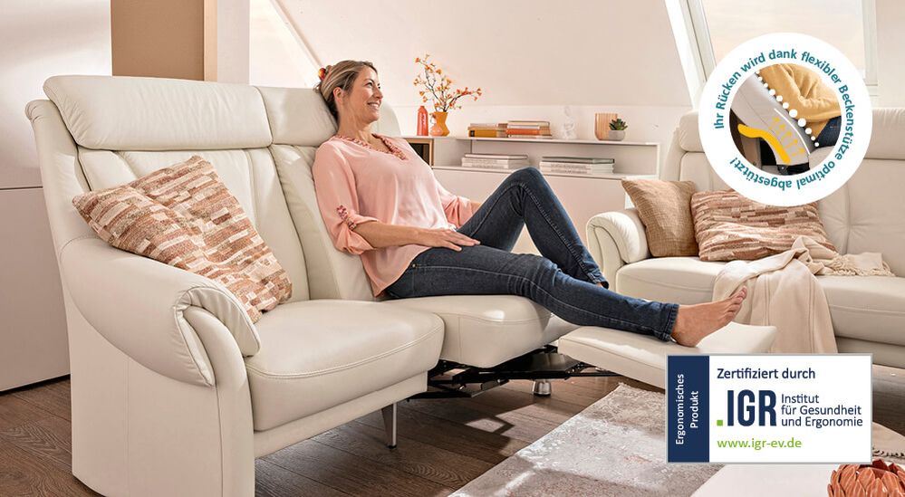 Eine Frau sitzt auf einem weißen Ledersofa mit ausgezogener Fußablage.