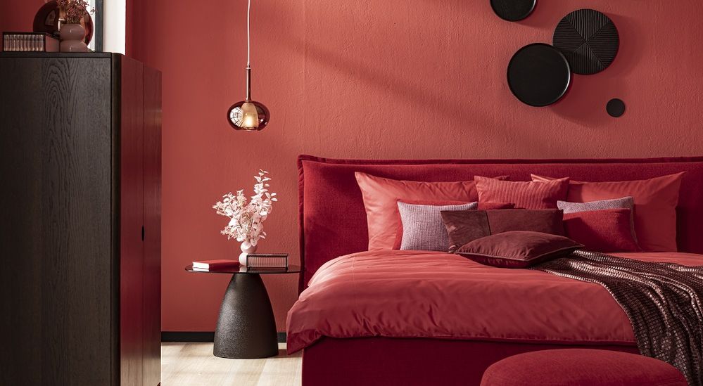 Rotes Schlafzimmer mit stilvoller Dekoration, roten Kissen auf einem Bett, hängender Lampe und dunklem Schrank, modernes und gemütliches Ambiente.