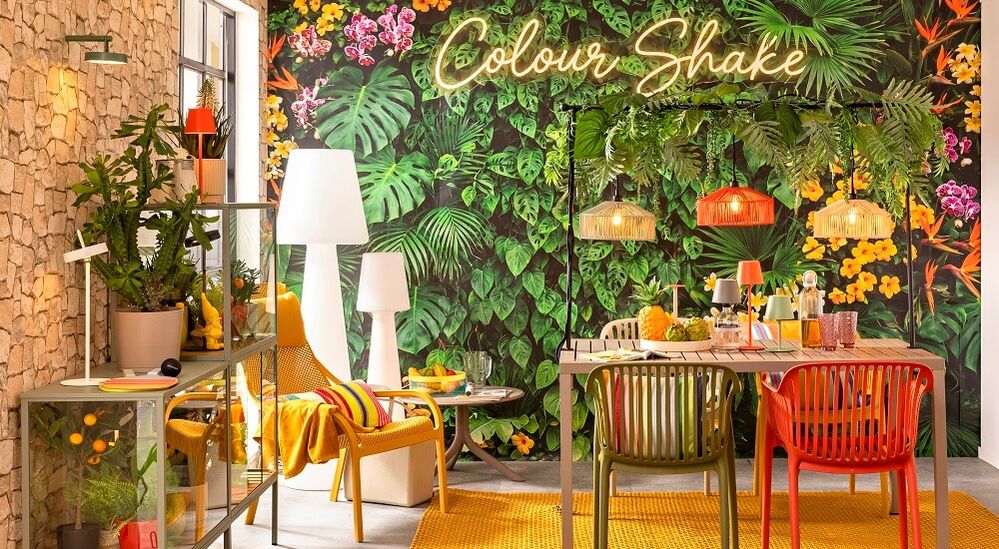 Lebendige Terrasse mit tropischer Tapete, Neon-Schild „Colour Shake“, bunten Stühlen, Pendelleuchten und Pflanzen. Gemütliche, vielseitige Einrichtung.