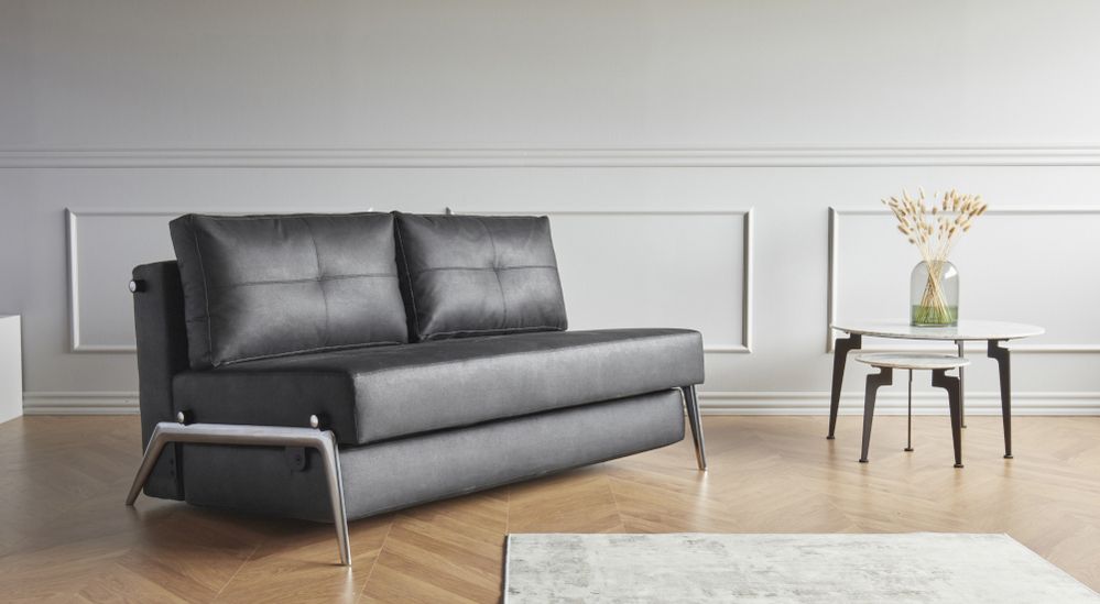 Dunkles Sofa mit zwei Kissen in einem hellen Raum mit weißer Wandverkleidung und einem runden Beistelltisch.