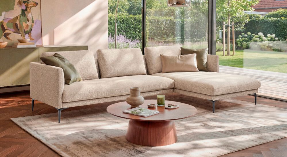Modernes Wohnzimmer mit beigem Sofa, Holztisch, Kunstwerk an der Wand. Große Fenster bieten Blick auf einen gepflegten Garten.