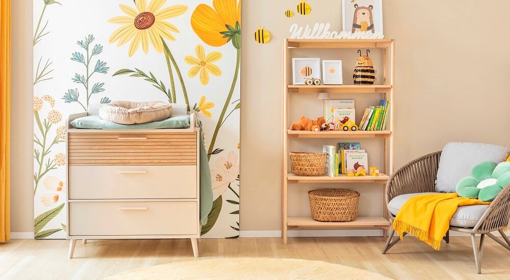 Freundlich gestaltetes Babyzimmer mit hellen Möbeln, bunter Blumentapete, gemütlichem Lesesessel und Bienen-Motiven.