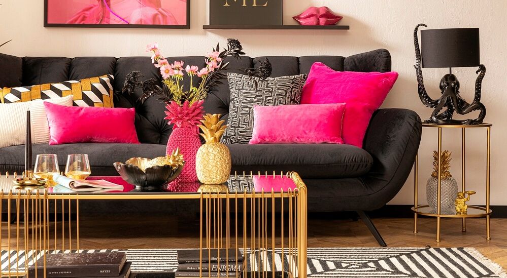 Stilvolles Wohnzimmer mit dunklem Sofa, leuchtend pinkfarbenen Kissen, Ananas-Dekoration und eleganten Kunstwerken an den Wänden.