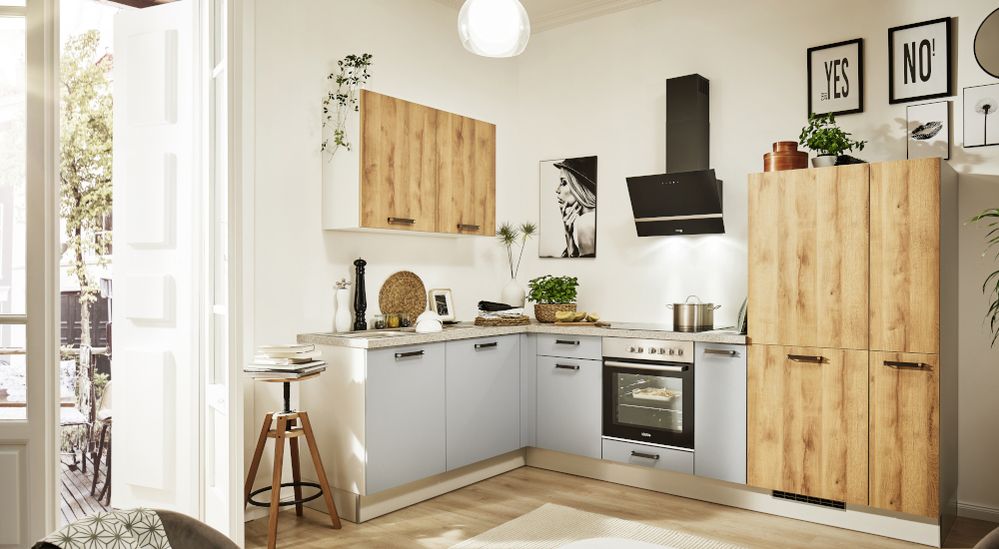 Helle, L-förmige Küche mit hellen Holzschränken und grauen Unterschränken, Edelstahl-Backofen und Dunstabzugshaube, Topfpflanzen, Holzhocker und gerahmten Wandbildern.
