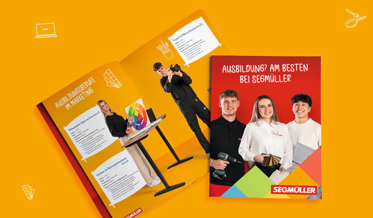 Aufgeschlagene Segmüller-Broschüre mit Personen, die Werkzeuge und eine Kamera halten und für Schulungsangebote werben. Leuchtend orangefarbener Hintergrund mit Symbolen.