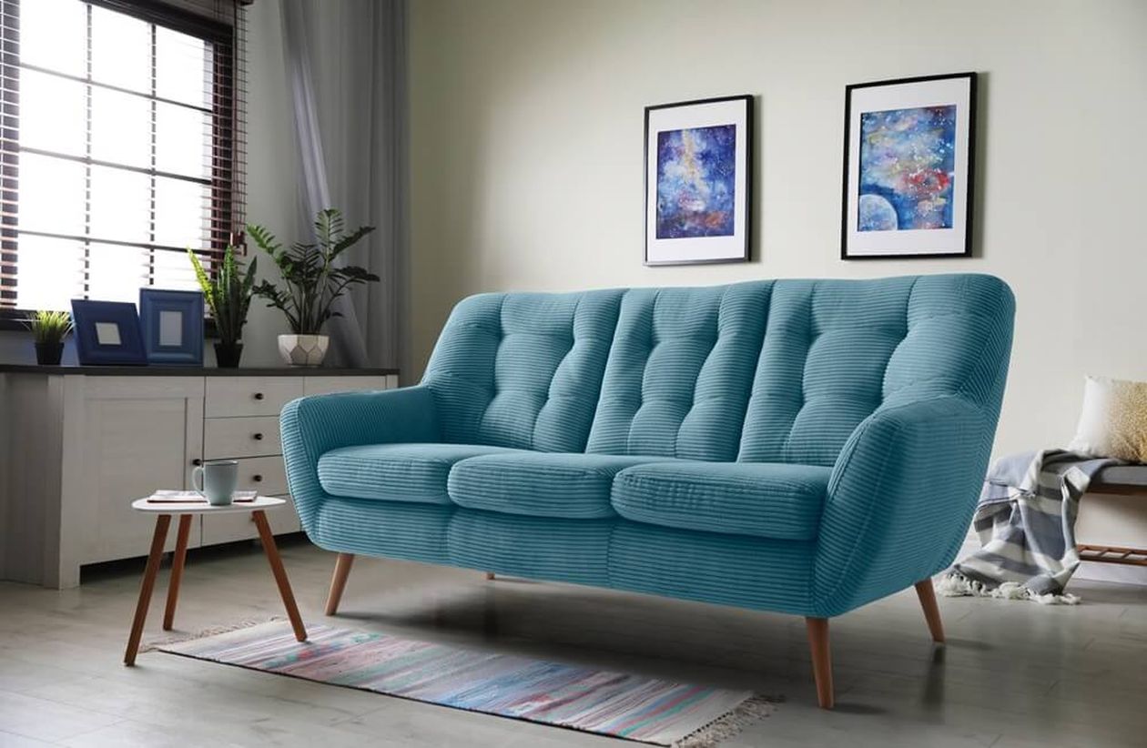 Türkisblaues Dreisitzer-Sofa im Retro-Stil mit Cord-Bezug und Holzbeinen in einem Wohnzimmer. Daneben ein kleiner Beistelltisch und Wandbilder mit Weltraummotiven.