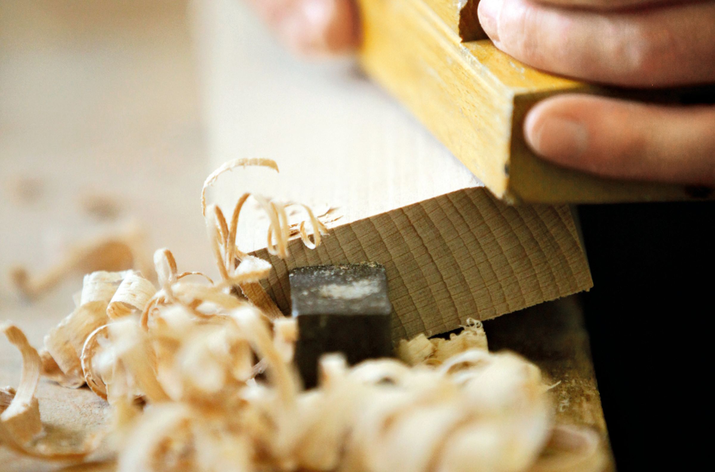 Nahaufnahme eines Balkens, der mit einem Hobel bearbeitet wird.