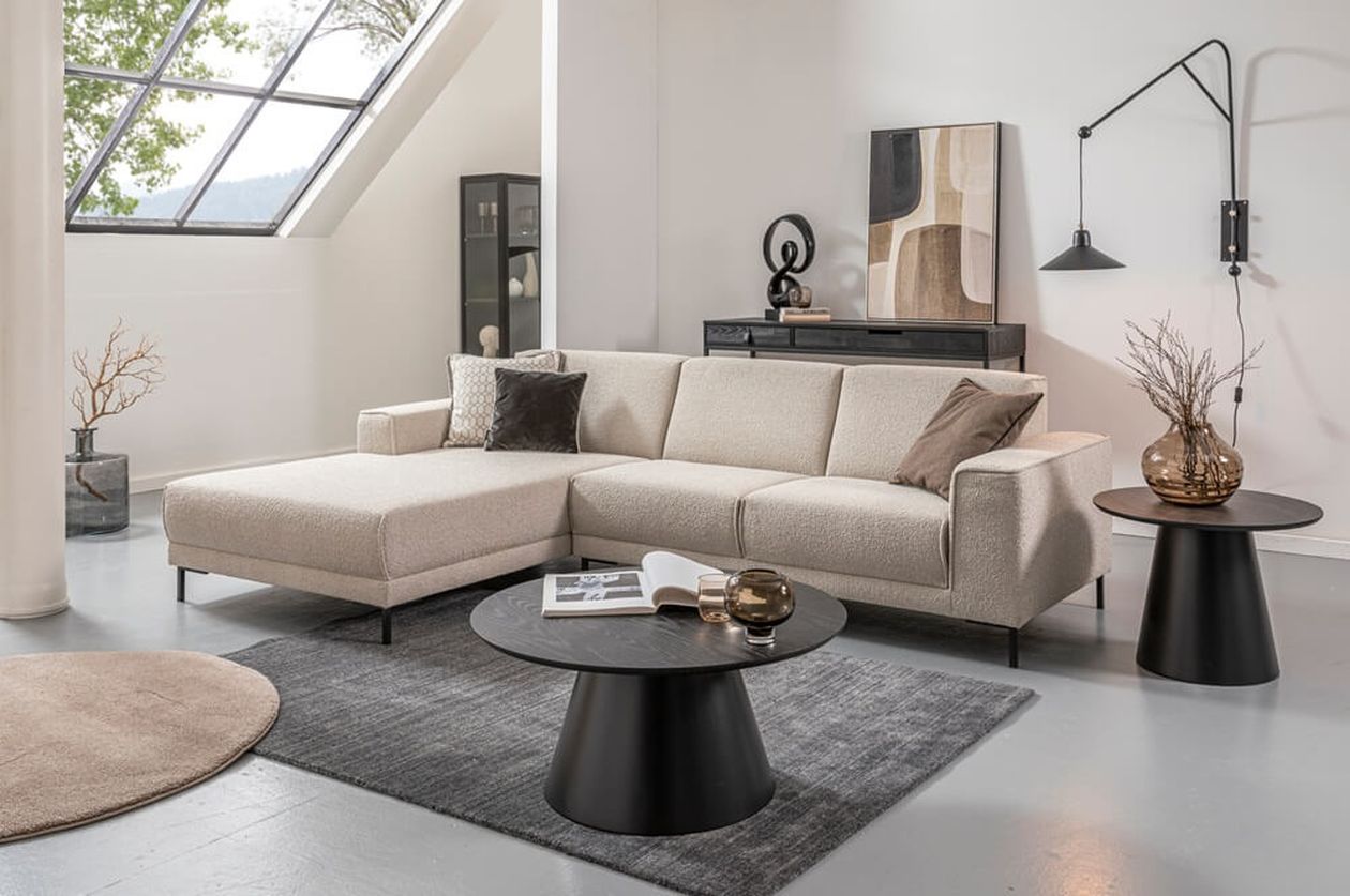 Cremefarbenes Ecksofa mit Récamiere links in einem modernen Wohnzimmer mit Dachschräge, schwarzen Couchtischen und minimalistischer Dekoration in Schwarz und Beige.