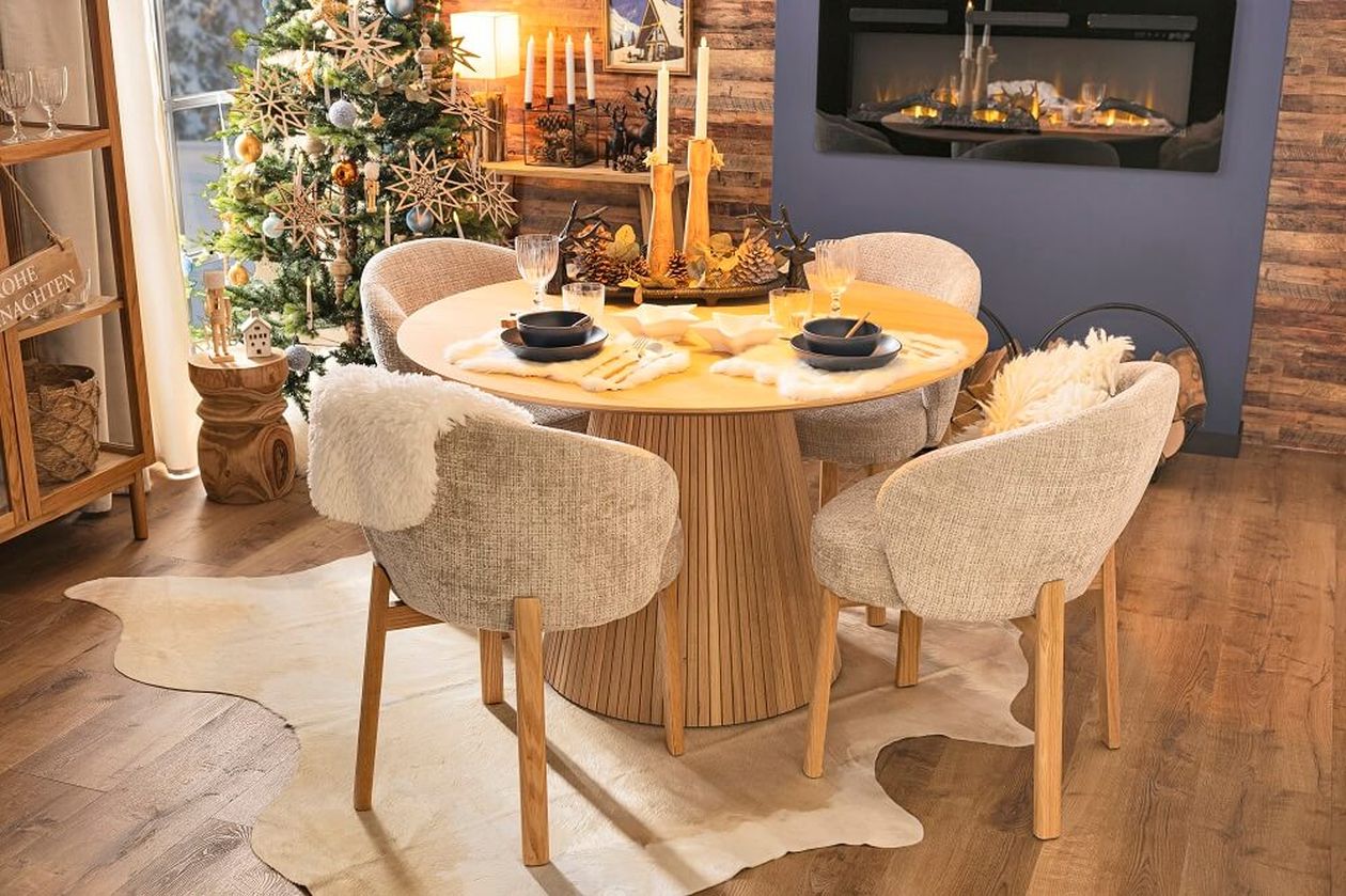 Gemütlicher Essbereich mit einem runden Holztisch, gepolsterten Stühlen, Weihnachtsdekoration, brennenden Kerzen und einem Weihnachtsbaum neben einem modernen Kamin.