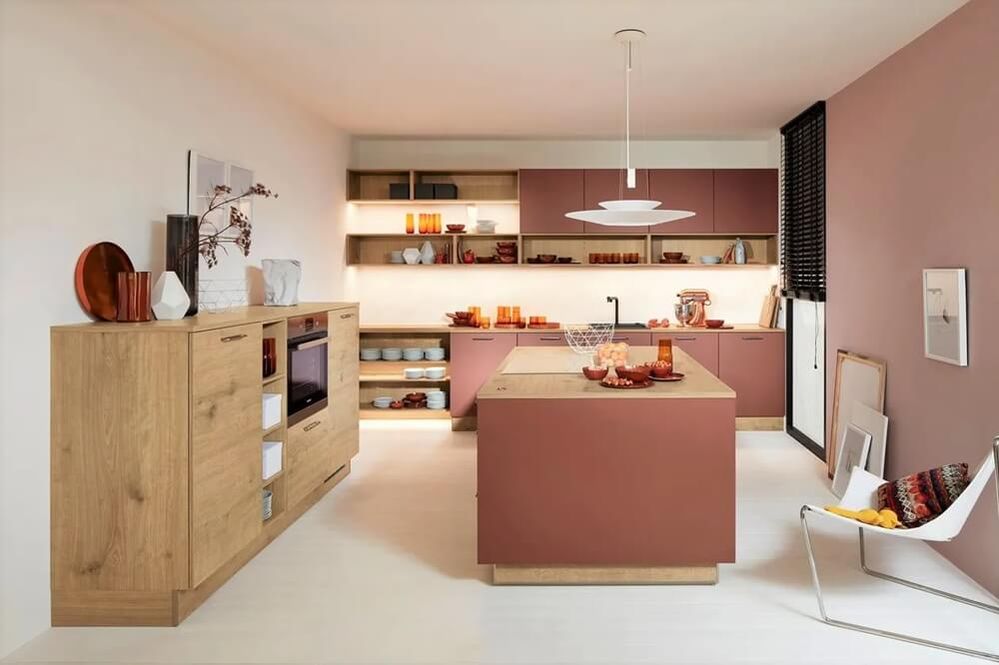 Moderne, offen gestaltete Küche mit Kochinsel in warmen Beigetönen und Altrosa. Offene Regale und dekorative Elemente wie Vasen und Geschirr sorgen für eine gemütliche Atmosphäre.