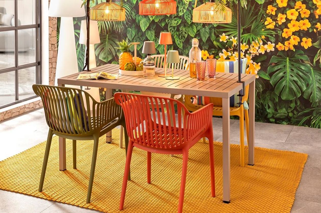 Ein lebhafter Essbereich mit Holztisch, farbenfrohen Stühlen, tropischer Dekoration und üppiger Pflanzenkulisse, begleitet von hängenden Weidenlichtern.