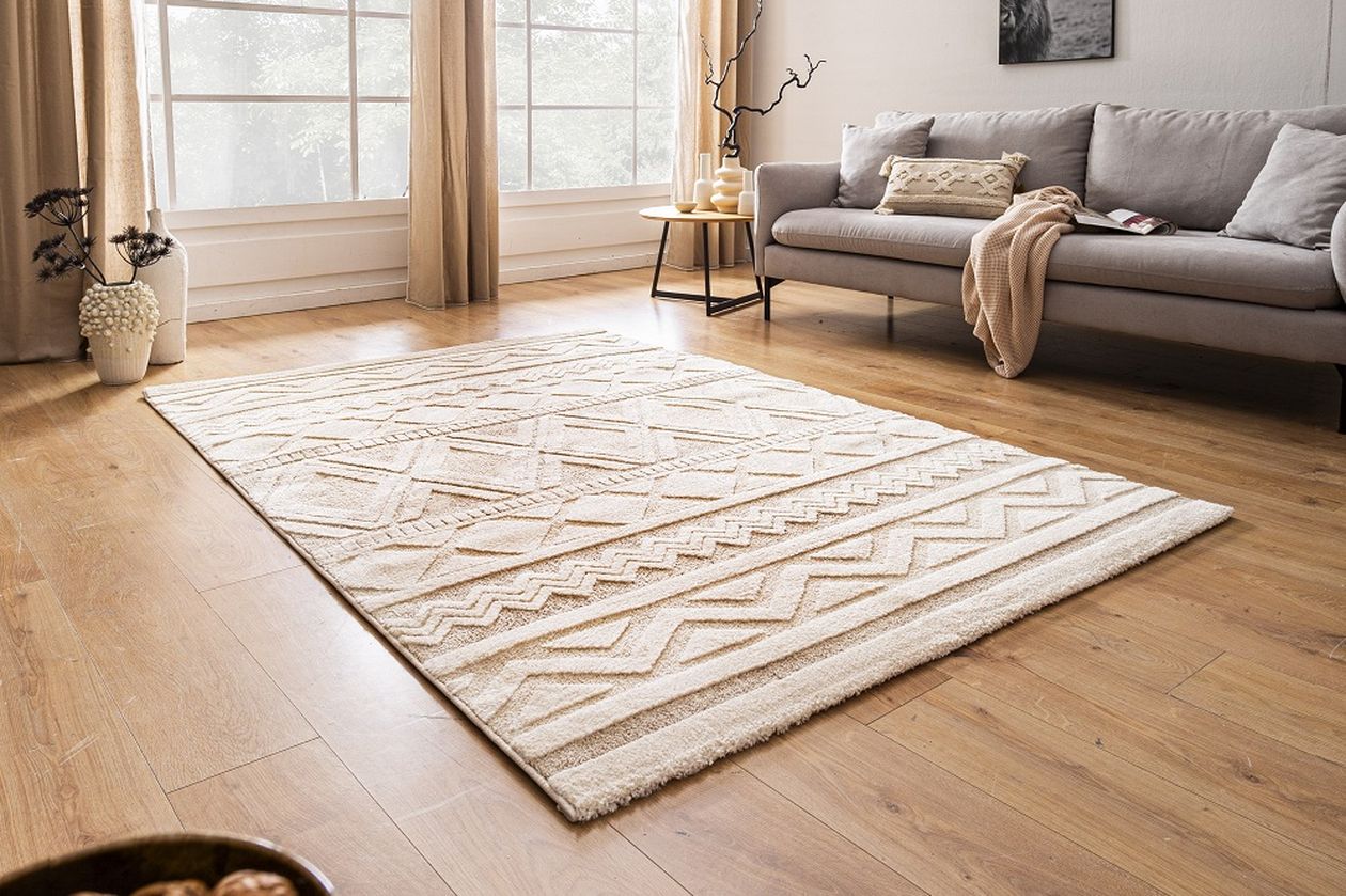 Ein helles Wohnzimmer mit einem großen cremefarbenen Teppich, einer grauen Couch, Holzboden und einem Beistelltisch mit Dekoration.