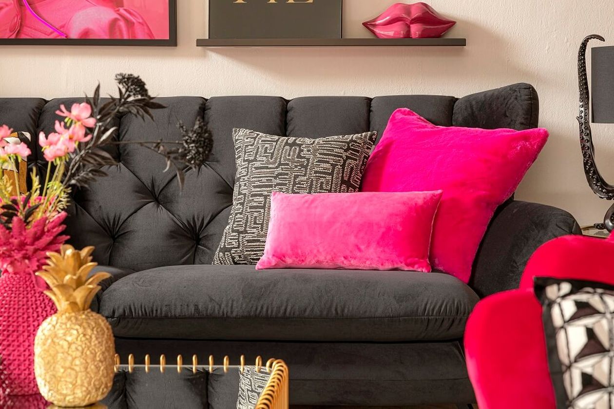 Stilvolles Wohnzimmer mit dunklem Sofa, leuchtend pinkfarbenen Kissen, Ananas-Dekoration und eleganten Kunstwerken an den Wänden.