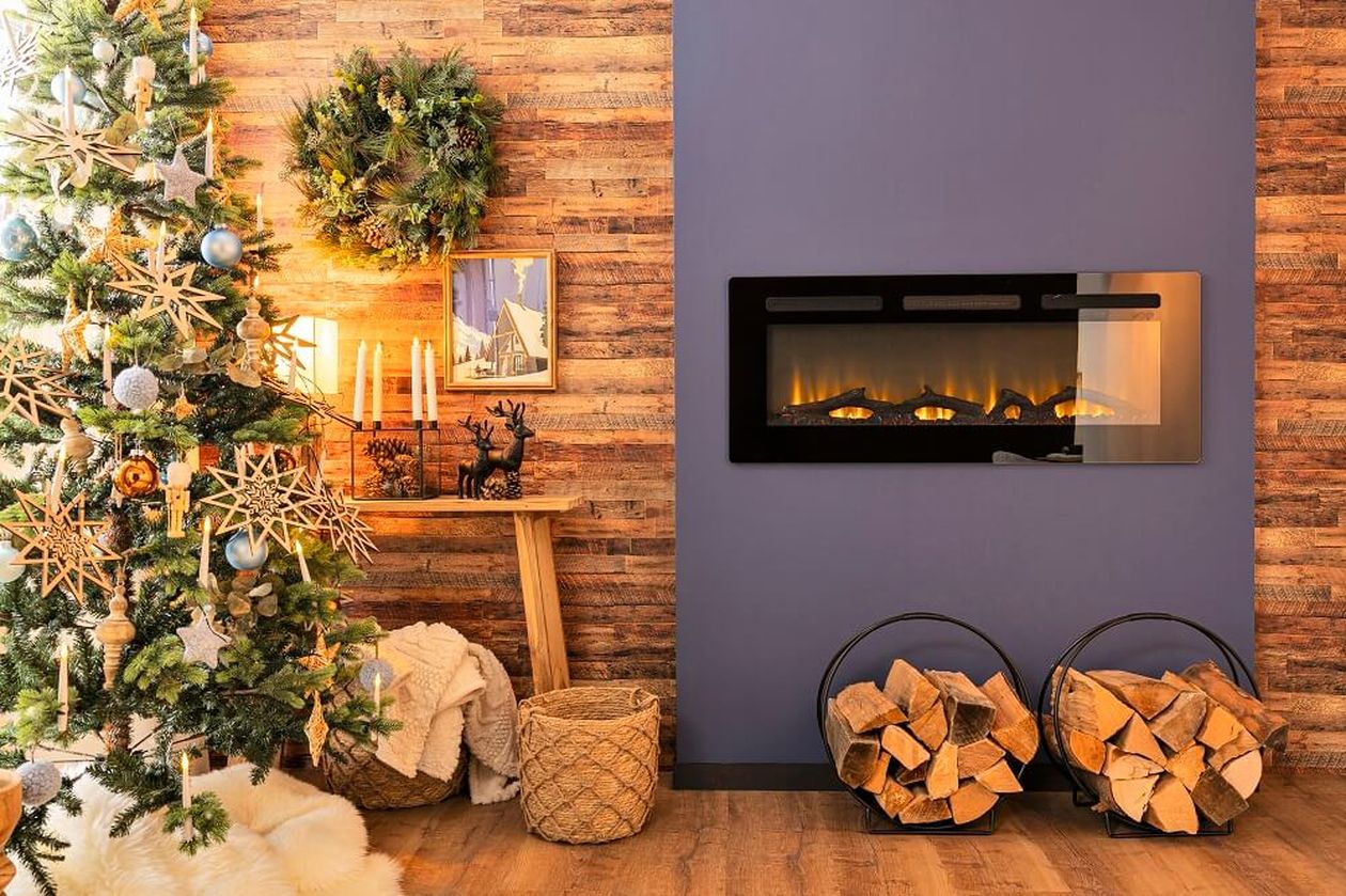 Gemütliches Zimmer mit geschmücktem Weihnachtsbaum, Wandkamin, Brennholz und festlicher Dekoration auf einem Holztisch.
