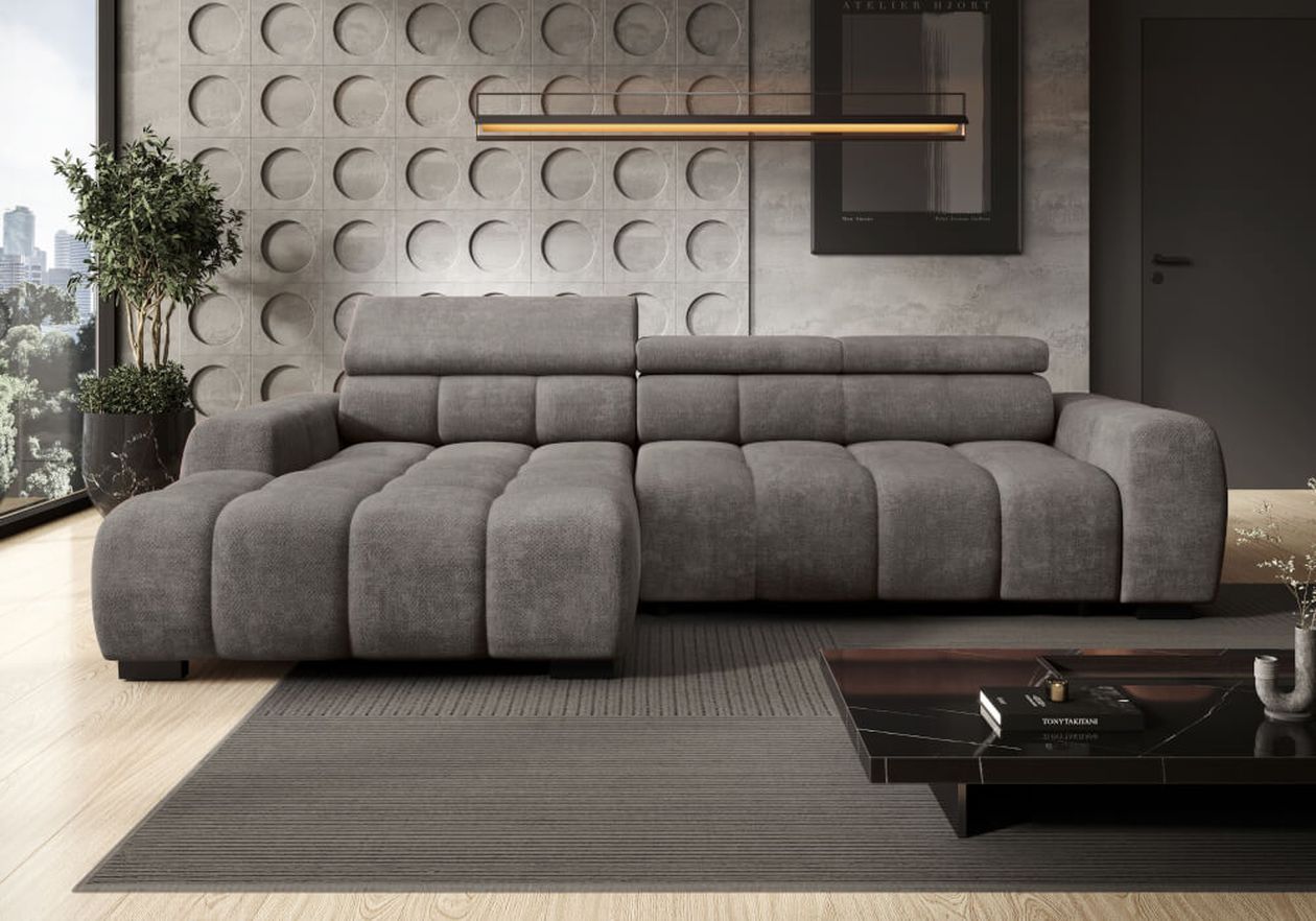 Ein modernes Wohnzimmer mit einem großen grauen Samt-Ecksofa, einer strukturierten Wand, einer geometrischen Deckenleuchte und einem dunklen Couchtisch auf einem grauen Teppich.