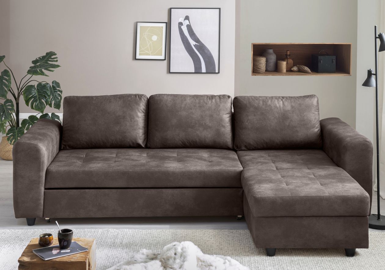 Braunes Ecksofa in einem gemütlichen Wohnzimmer mit moderner Kunst, einer Stehlampe, einer Pflanze und einem Regal mit Dekoartikeln. Im Vordergrund ein Couchtisch mit Tassen.