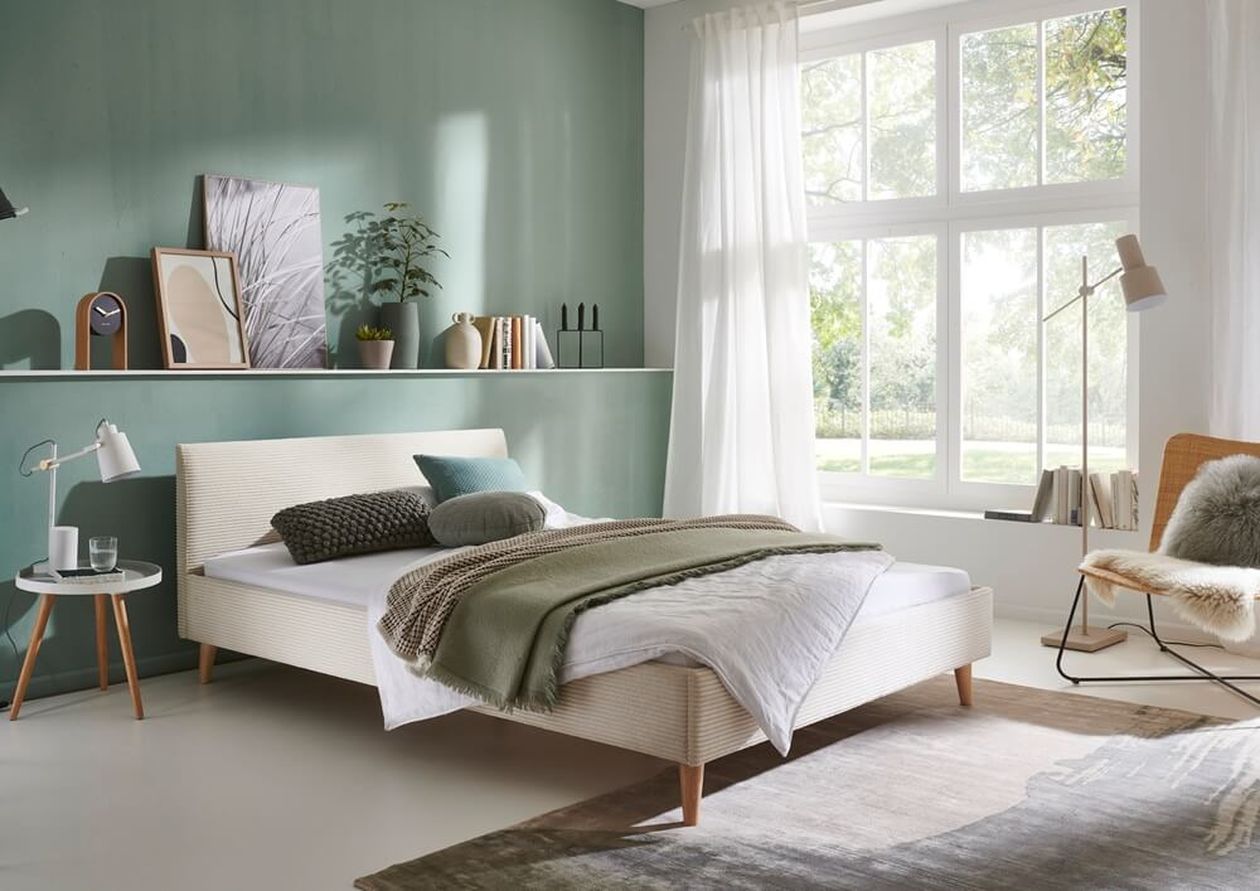 Helles, modernes Schlafzimmer mit einer grünen Akzentwand, minimalistischer Einrichtung, einem gemütlichen Bett und einem großen Fenster, das natürliches Licht hereinlässt.