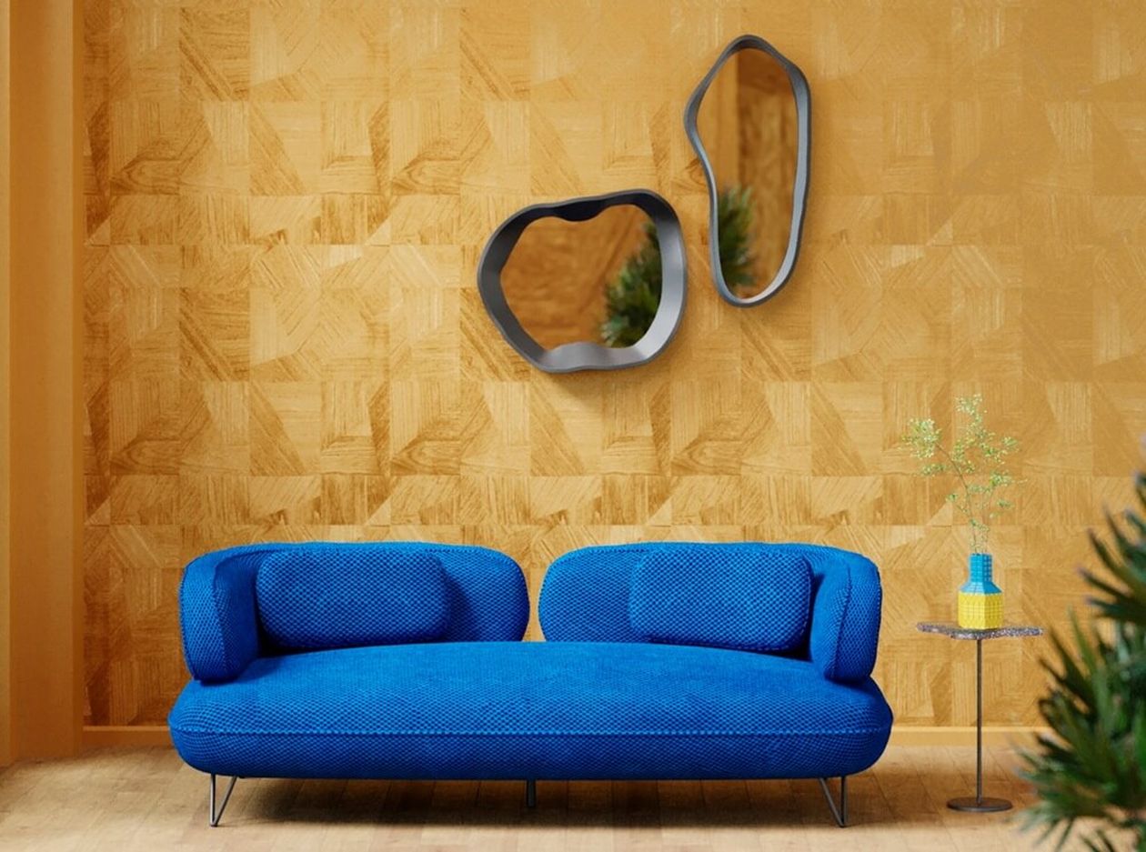 Auffälliges blaues Sofa mit organisch geschwungener Form und strukturiertem Stoffbezug vor einer goldgelben Wand mit zwei organisch geformten Spiegeln mit grauen Rahmen.