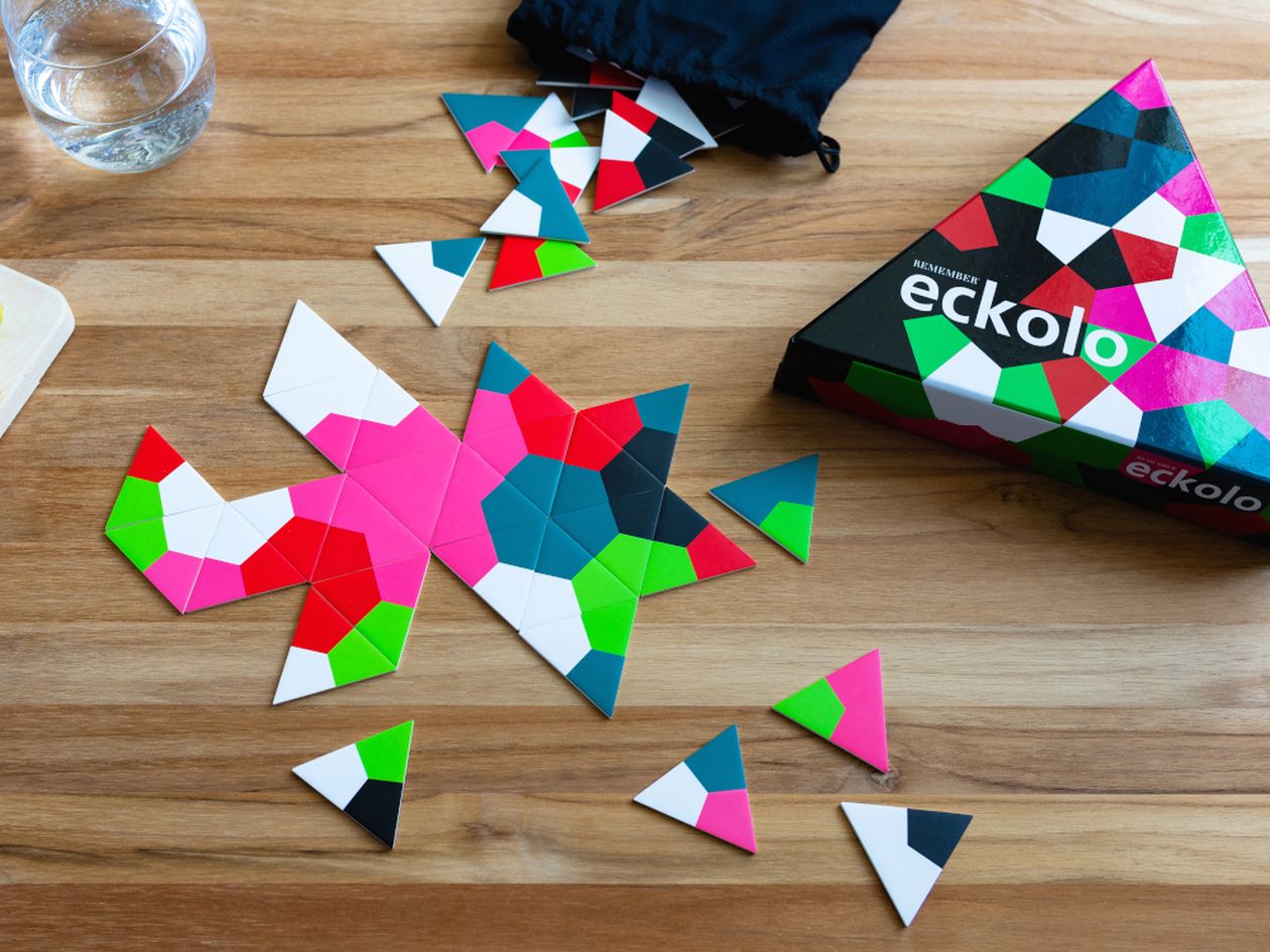 Die Box und bunte Spielsteine der Spiels Spiel Eckolo von Remember liegen auf einem Holztisch.