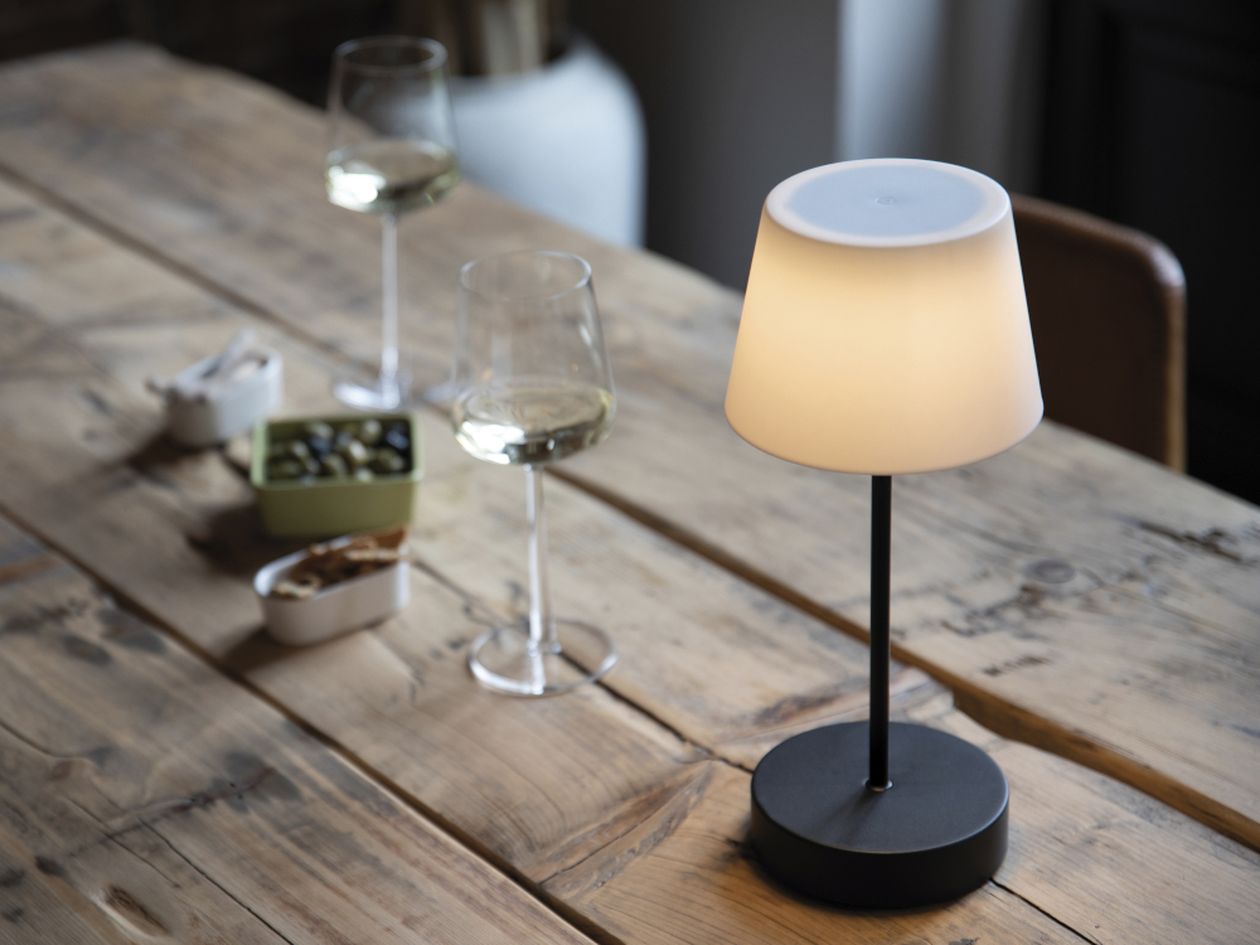 Die schwarze Akku-Tischleuchte Oscar Pure aus Aluminium von Remember steht auf einem Holztisch.