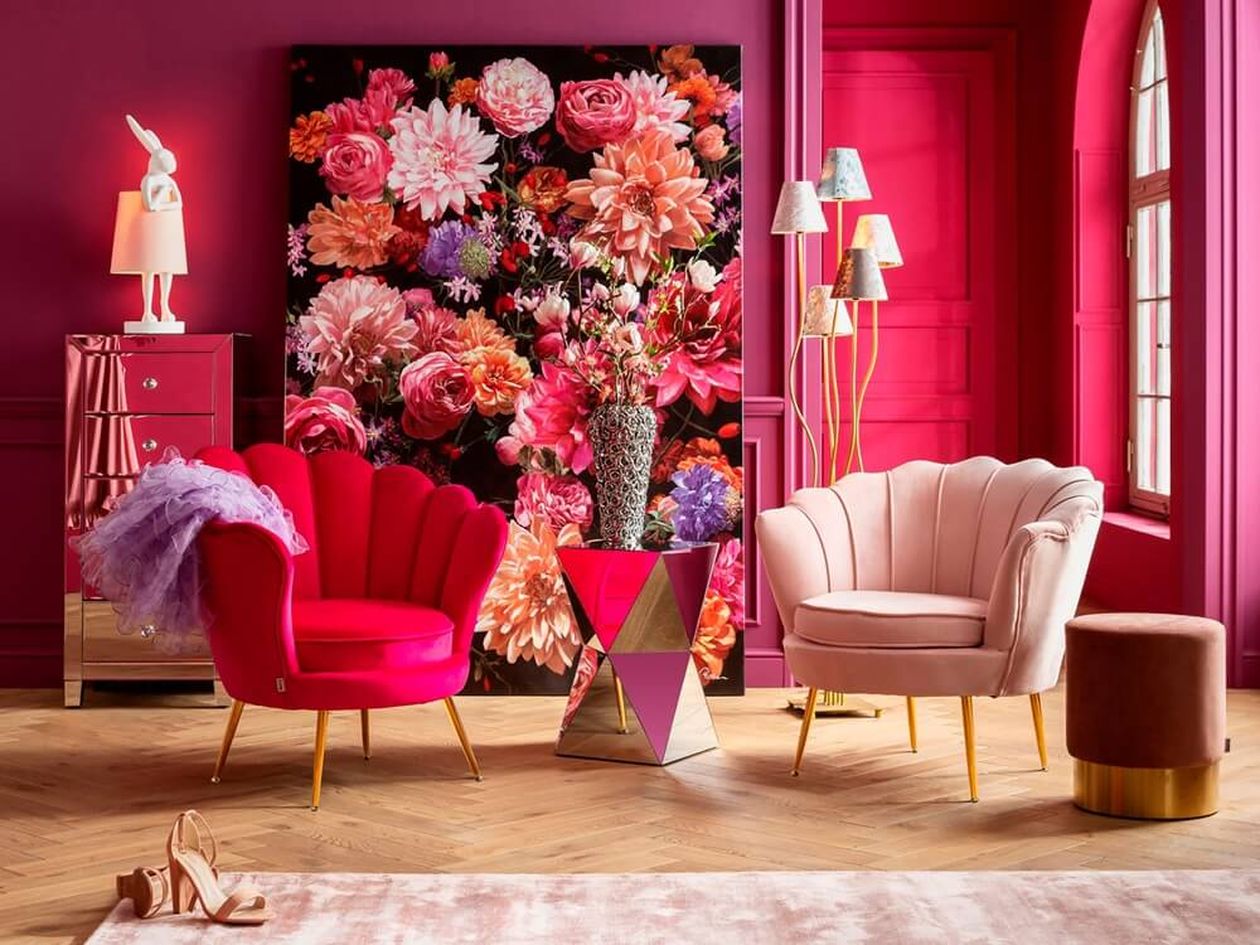 Zwei muschelförmige Samtsessel – einer in kräftigem Pink, einer in zartem Rosa – mit goldenen Beinen in einem pinkfarbenen Raum mit großem Blumengemälde und verspiegelter Kommode.