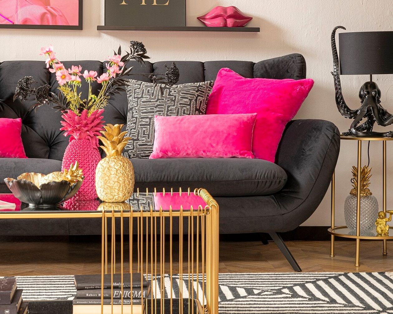 Stilvolles Wohnzimmer mit dunklem Sofa, leuchtend pinkfarbenen Kissen, Ananas-Dekoration und eleganten Kunstwerken an den Wänden.