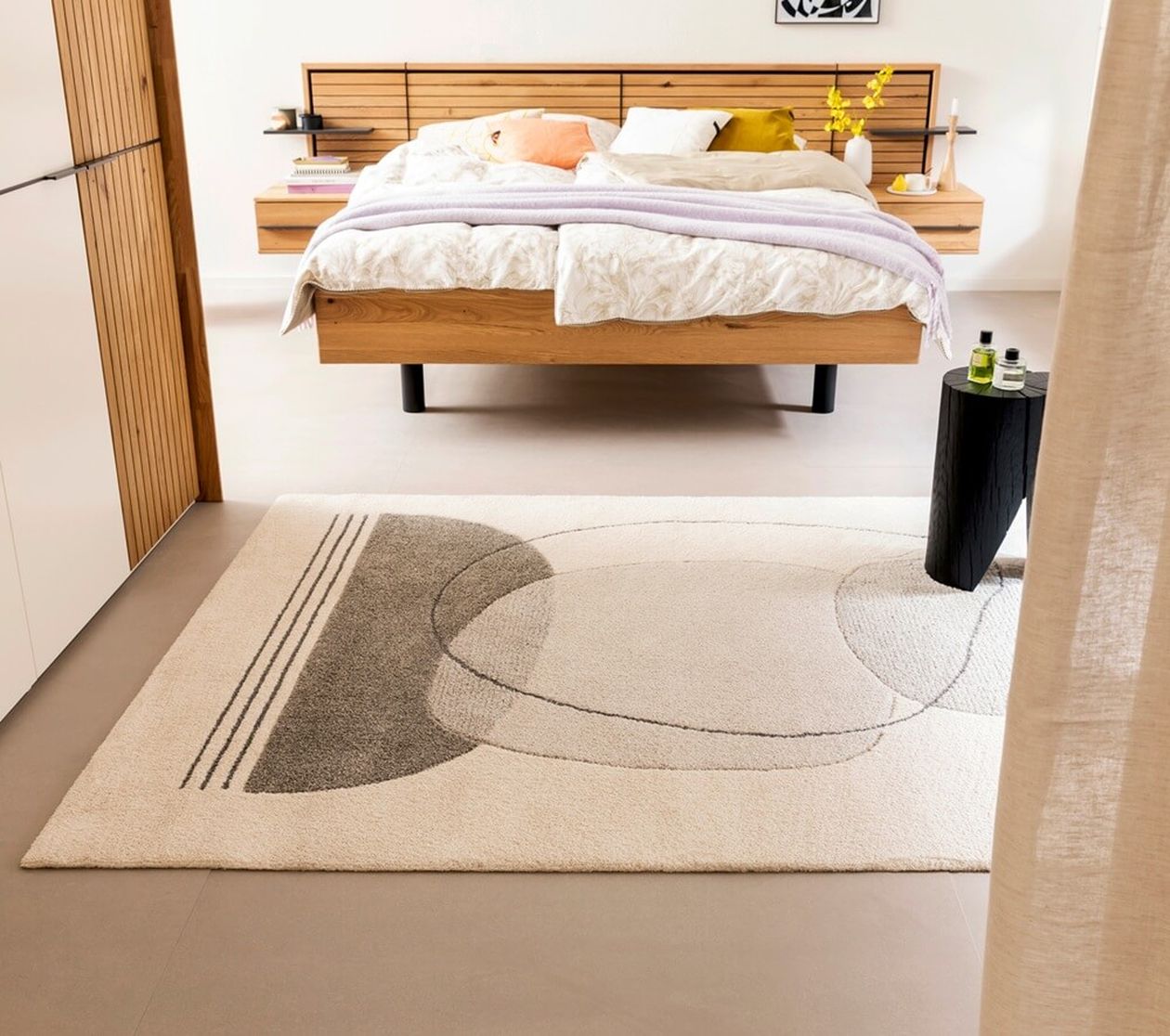 Heller Teppich mit abstrakten, grafischen Linienmustern liegt in einem minimalistisch eingerichteten Schlafzimmer.